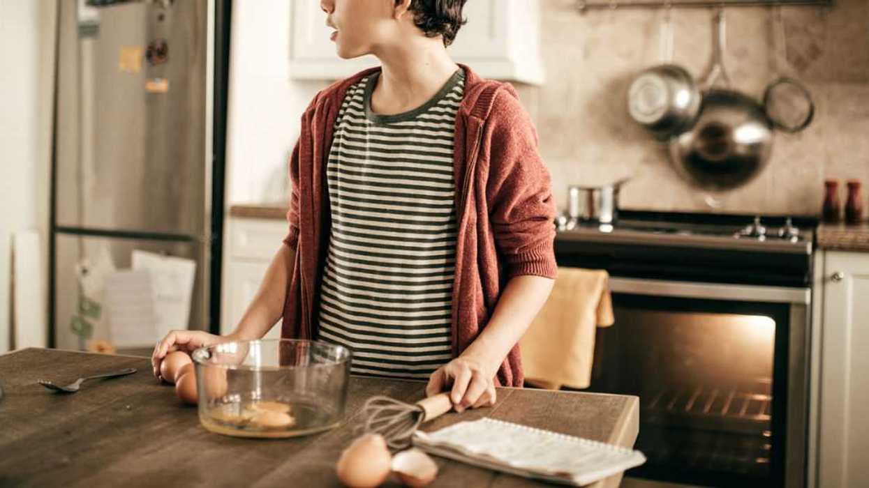 Teenager stands at kitchen island with a bowl of eggs in front of him.