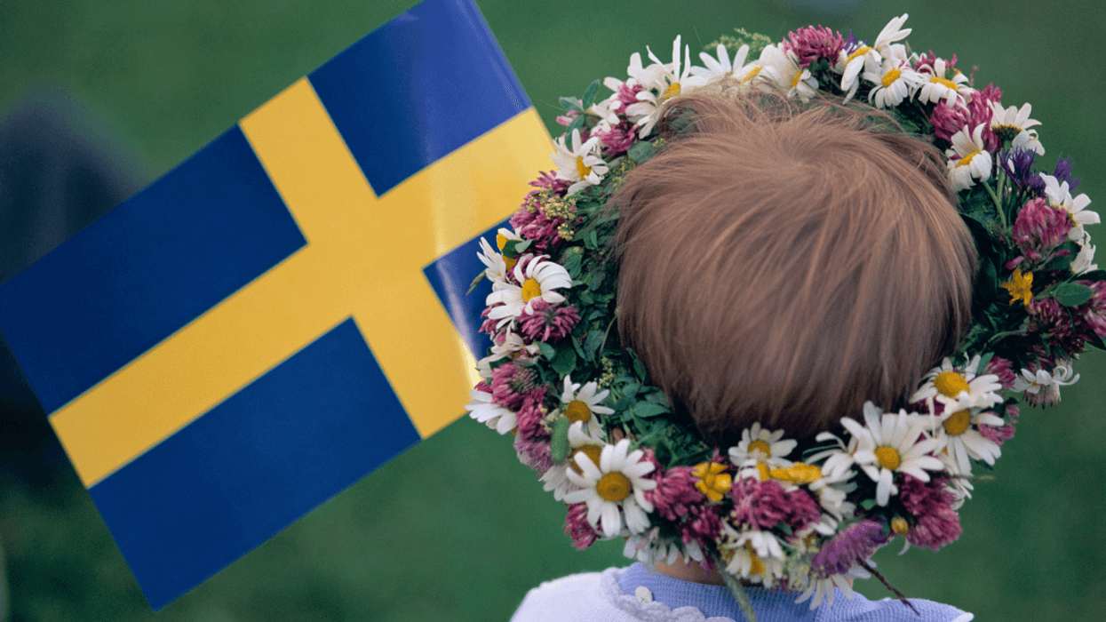 The back of the head of a child wearing a floral crown and holding a Swedish flag.