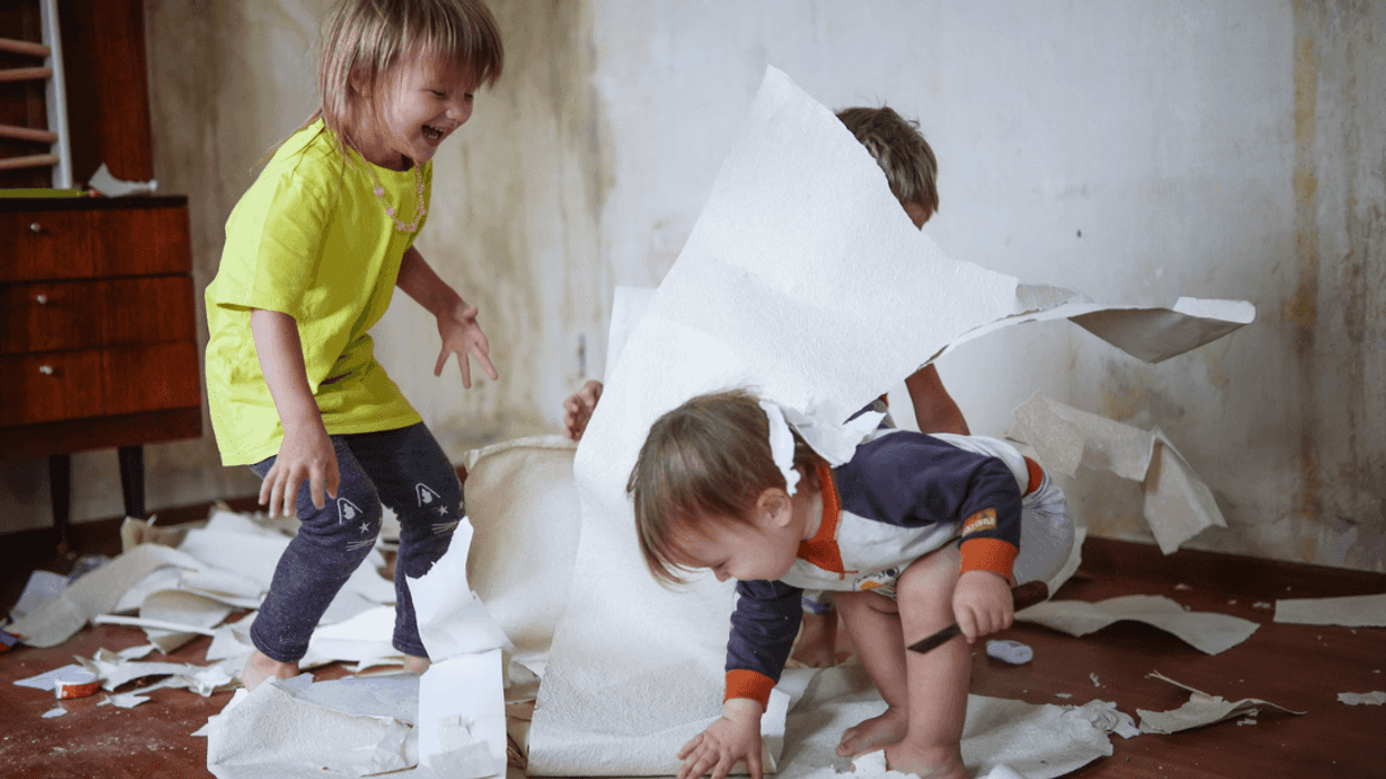 Three children throwing sheets of paper all over a room.