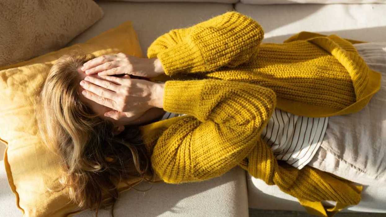 Tired woman lying on sofa while holding hands on her face.