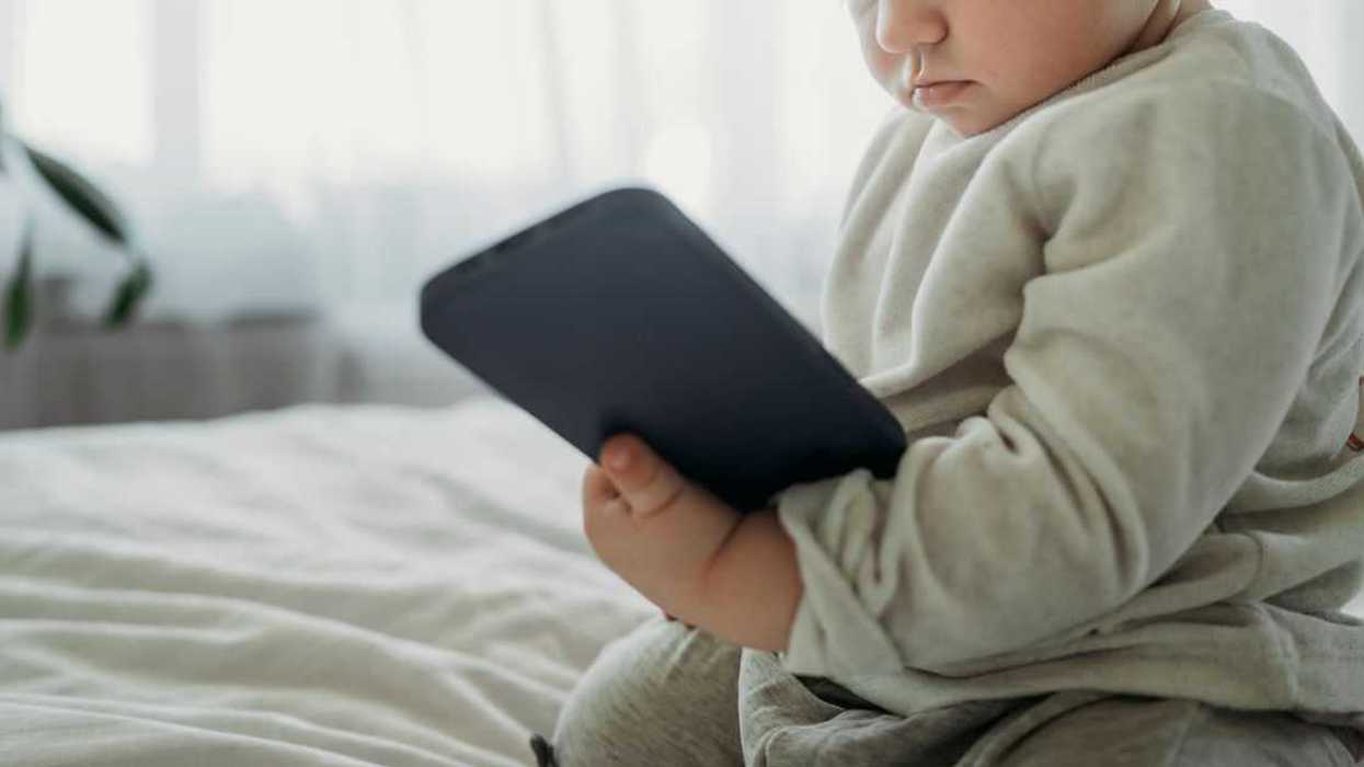 Toddler boy holding smart phone on bed at home.
