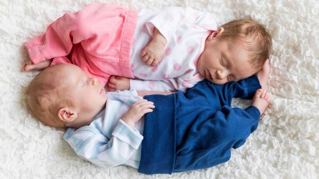 Two babies, a boy and girl, lay together on a white shag carpet