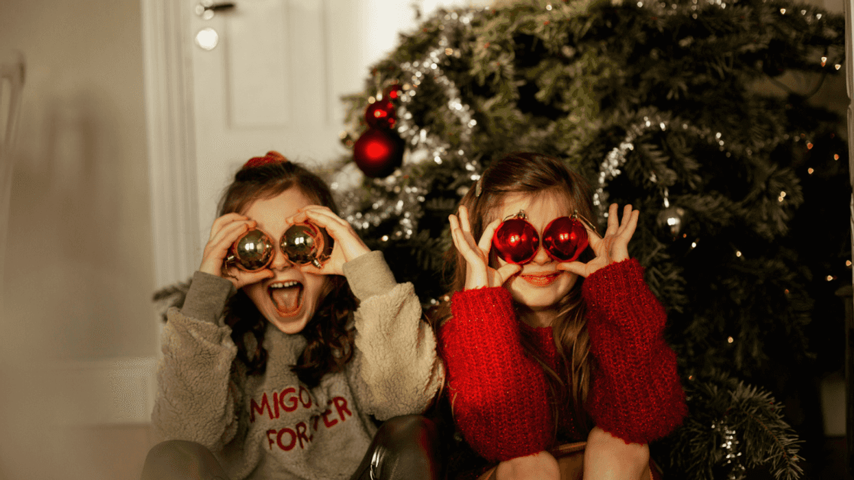 Two children sitting by a Christmas tree, covering their eyes with Christmas ornaments.