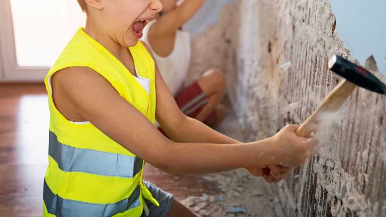 Two little manual workers renovating their room. Boys aged 7 are tearing out plaster from the walls using hammer and chisel.