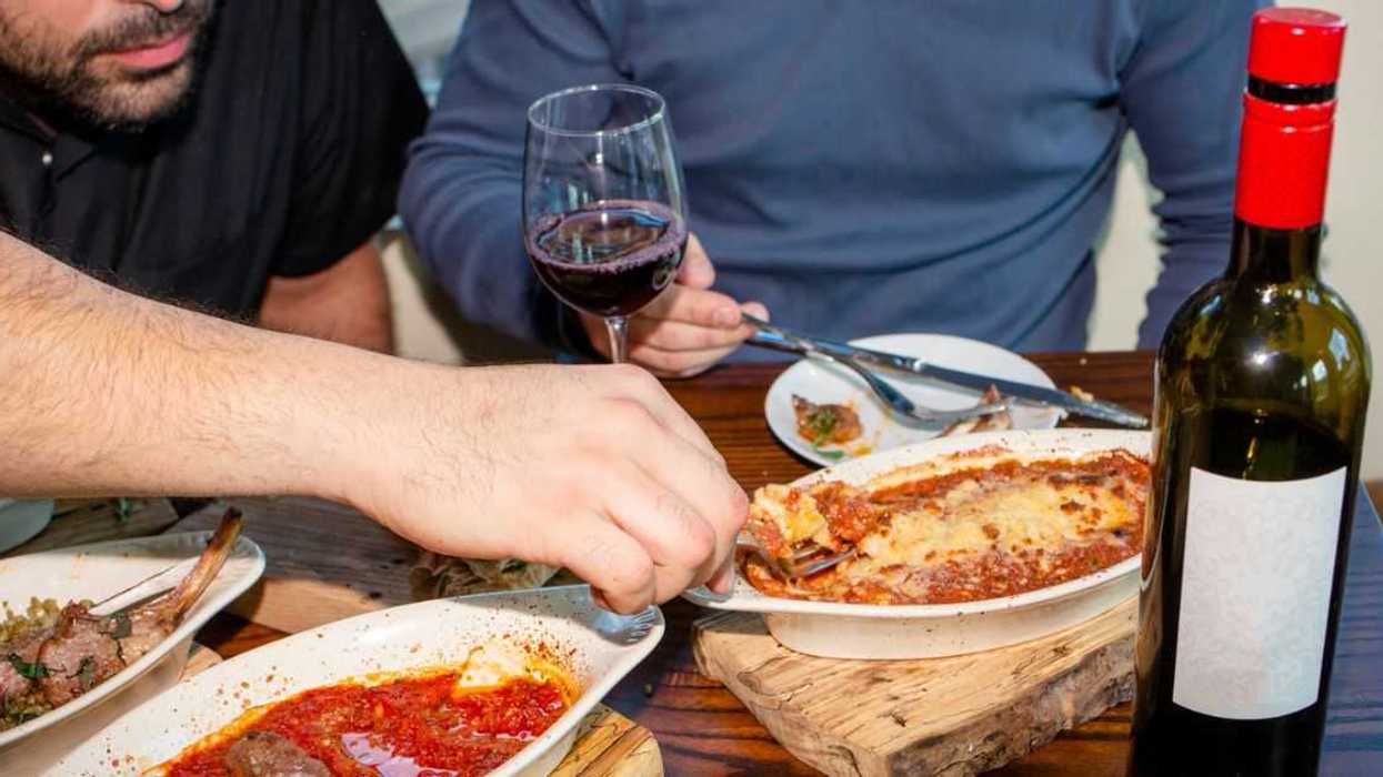 Two men eat lasagna and drink red wine