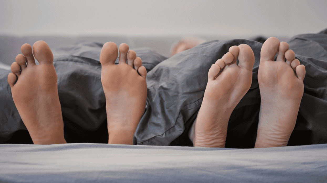 Two pairs of feet sticking out under a duvet on a bed.