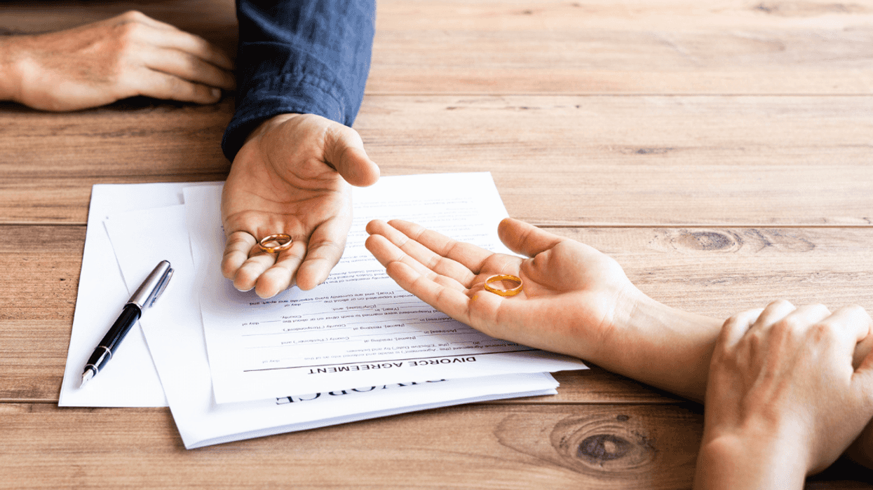 Two people holding wedding rings resting their hands on divorce papers.