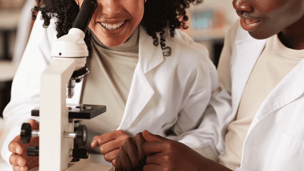 Two people in lab coats looking into a microscope.