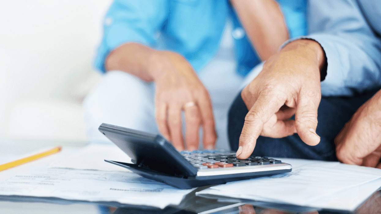 Two people looking at a calculator on a table over a pile of bills.