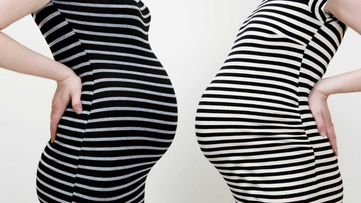 Two pregnant women in striped dresses face one another, stomach to stomach.