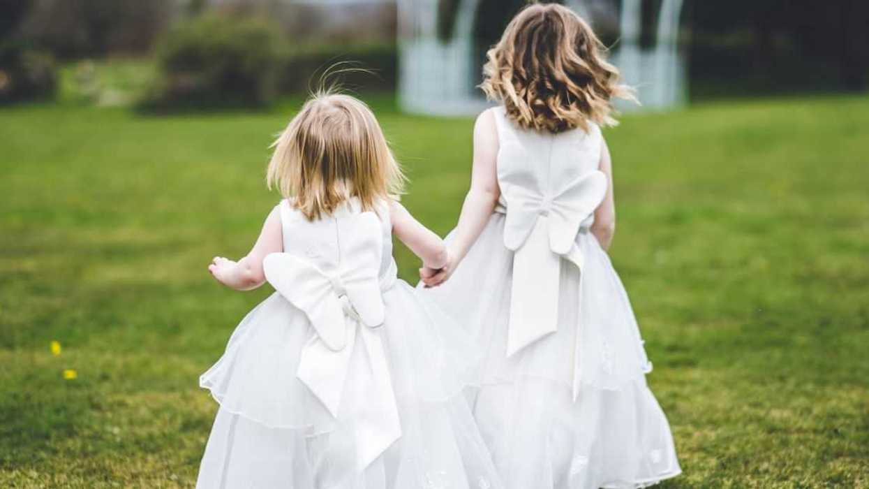 Two tiny Flower Girls run on the grass at a wedding.
