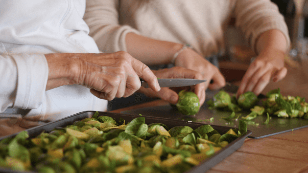 Two women cutting up brussell sprouts at a kitchen counter.
