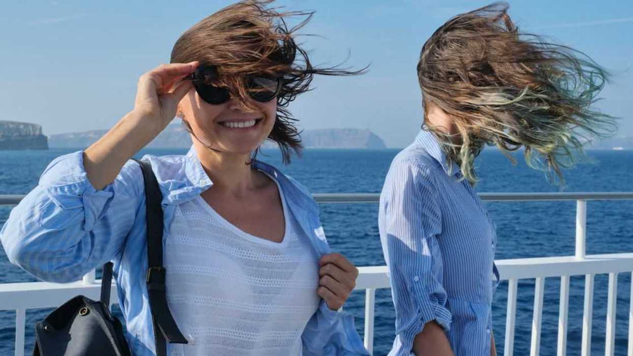 Two women enjoying sea travel on cruise ship, hair flying in the wind.