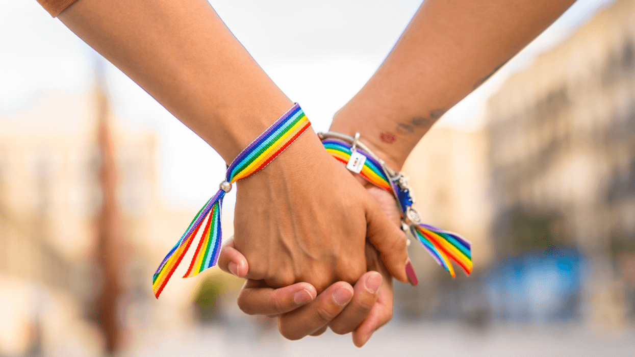 Two women holding hands wearing pride bracelets.