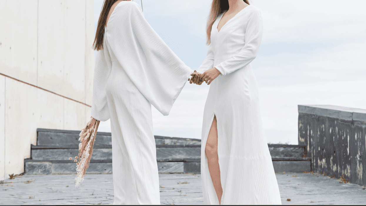 Two women in white gowns holding hands.