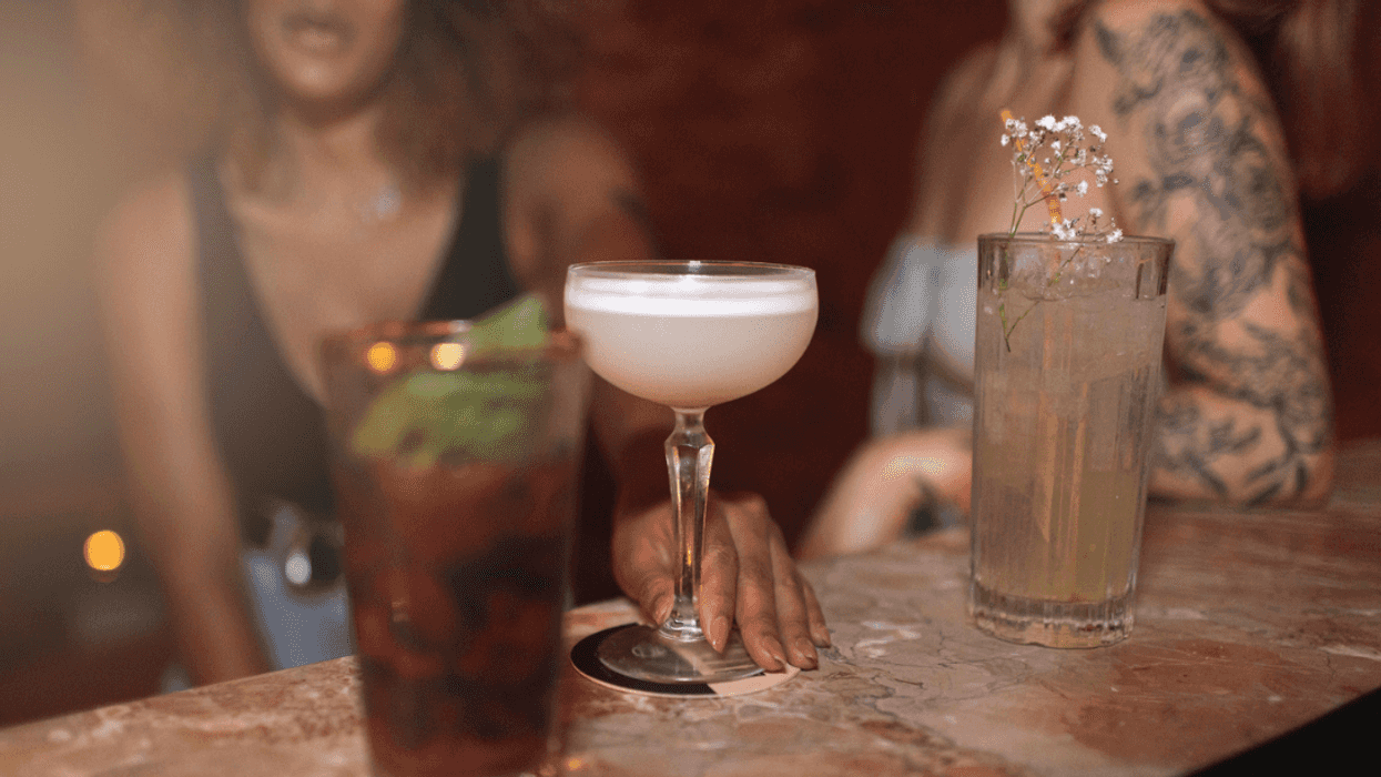 Two women sitting at a bar with three cocktails in front of them.
