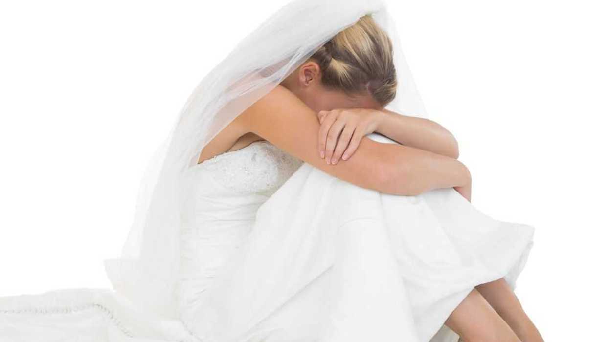 Unhappy blonde bride sitting on floor hiding her face.