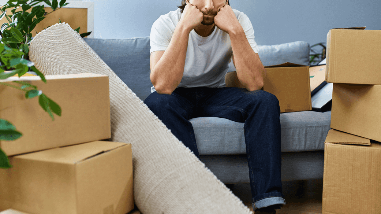 unhappy young man seated on couch surrounded by moving boxes