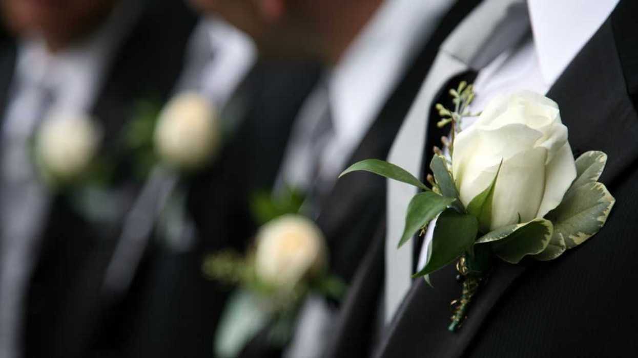 Unidentifiable groomsmen in black wearing white rose boutonnieres.