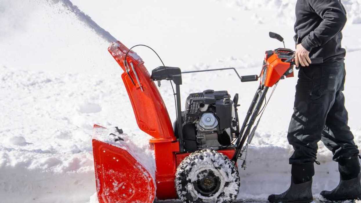 Unidentifiable man removing snow on the driveway of the house by snow blower.