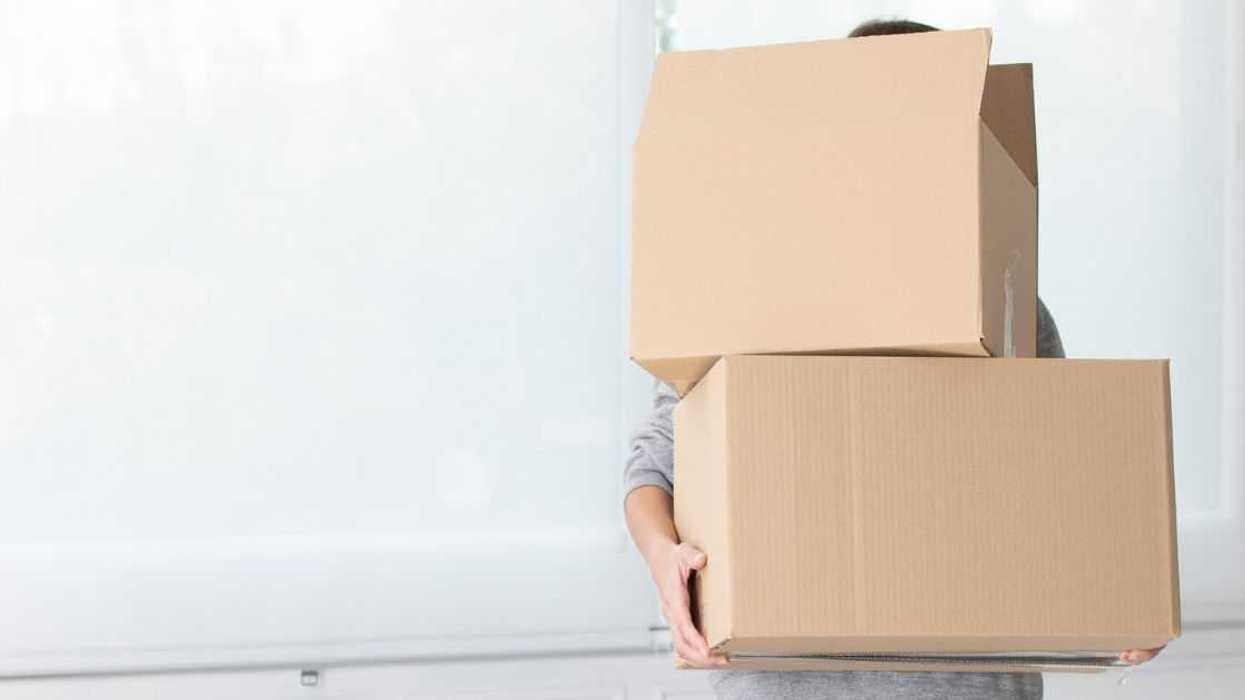 Unrecognizable woman carrying cardboard boxes in new home.