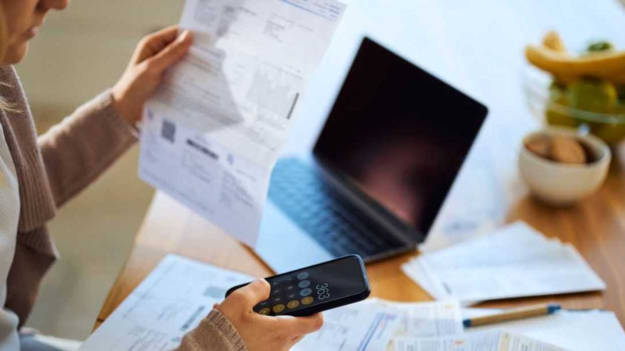Unrecognizable woman using mobile phone while calculating the amount of her bills at home. Focus is on hand and cell phone.