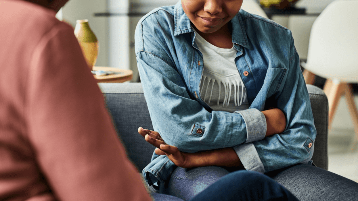 upset preteen girl seated on couch speaking to adult