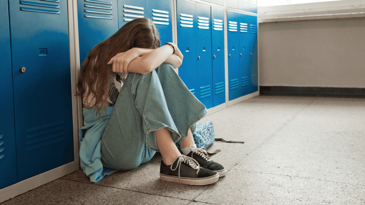 upset teenage girl seated in school hallway in front of lockers