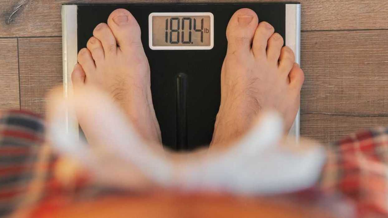 View from Above: Man Weighing In on Scale on Wooden Floor at Home.