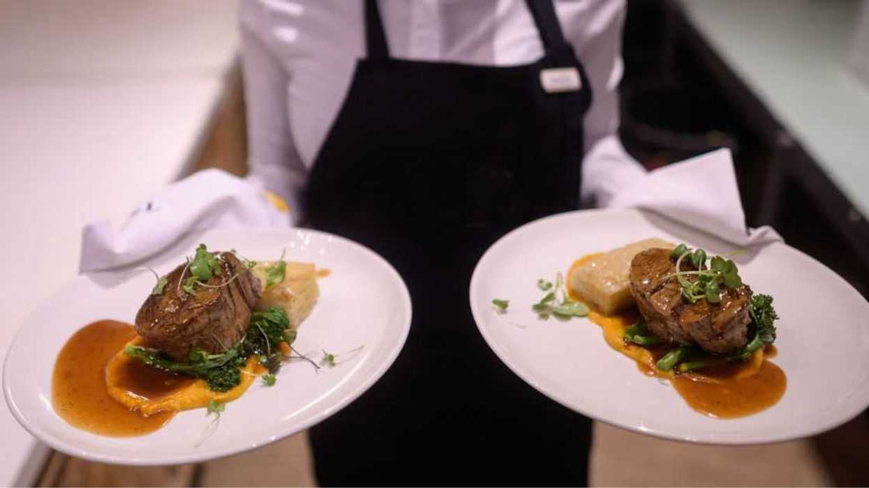 Waiter holding hot plated grilled steak and vegetables potatoes asparagus butter nut garnish sauce.