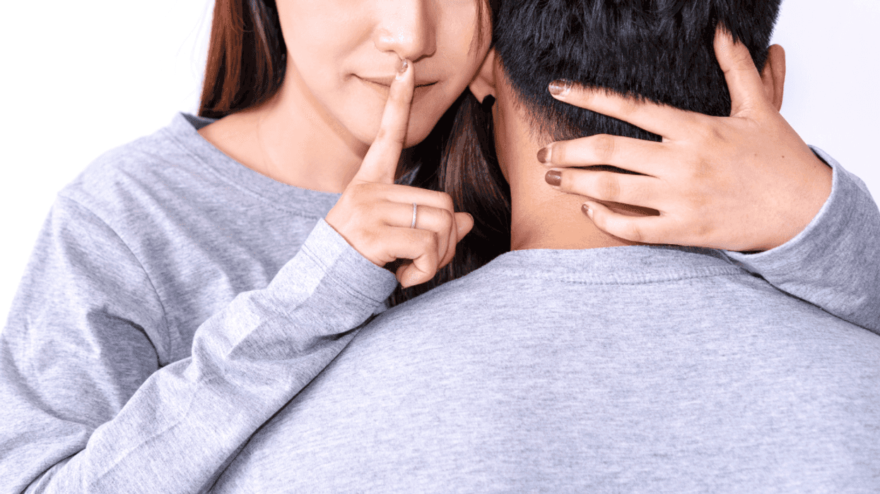 woman and man embrace as woman puts finger to lips to shush someone