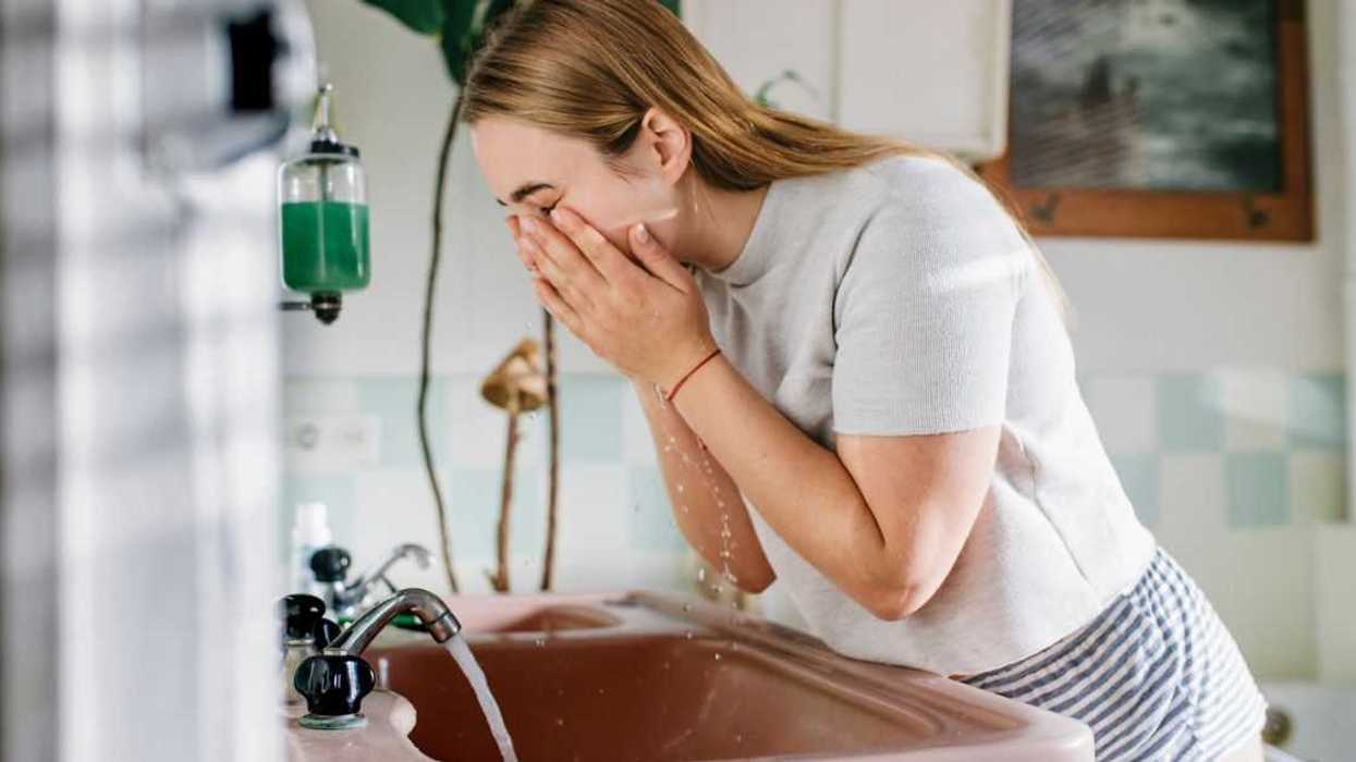 Woman bending over bathroom sink washing her face.