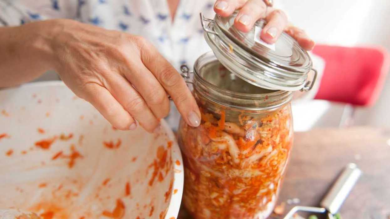 Woman closing the swivel top mason jar with all the mixed ingredients (and a weight) for a healthy fermented, originally Korean, side dish: kimchi.