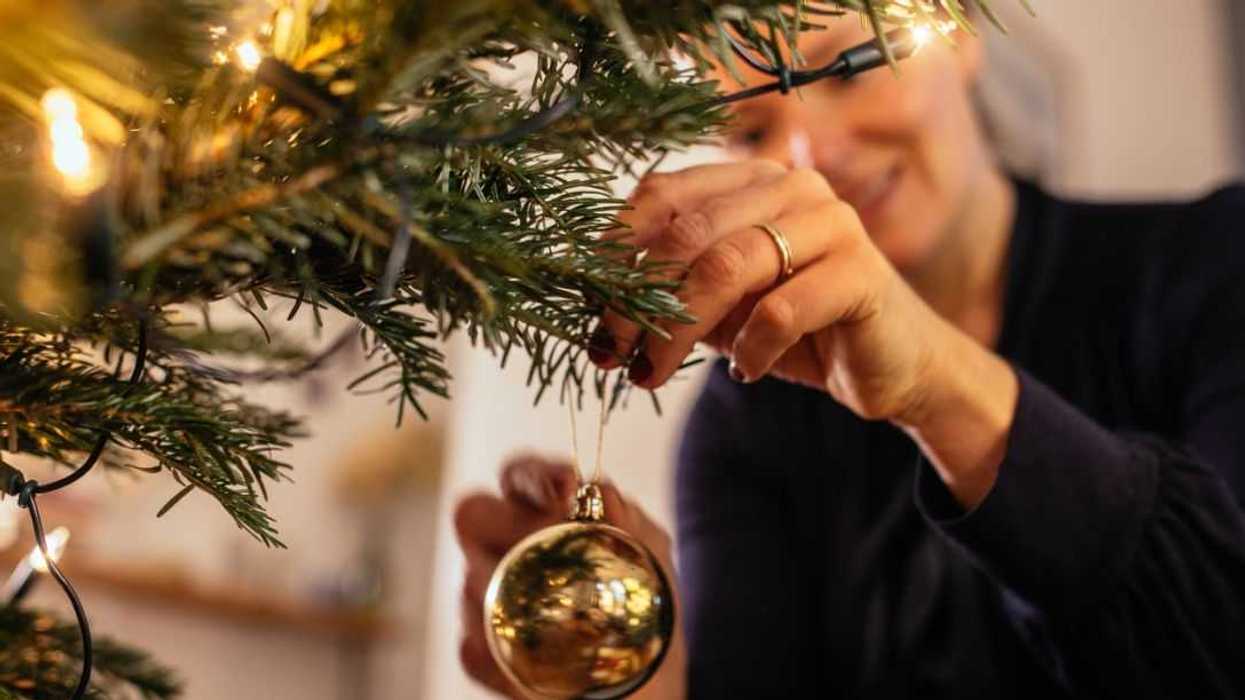 Woman decorating Christmas tree at home with golden Christmas tree decorations.