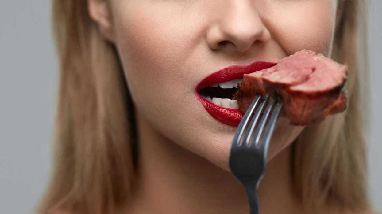 Woman Eating Meat. Closeup Of Beautiful Female Face Biting Meat