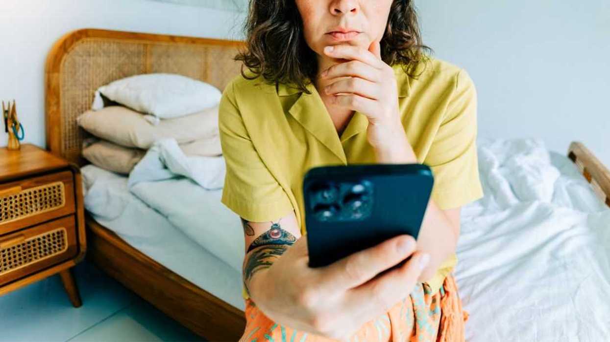 Woman feeling stressed, looking at smartphone in bedroom.