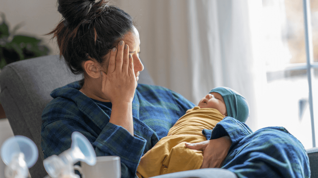 Woman holding a baby and resting her head in her hands.