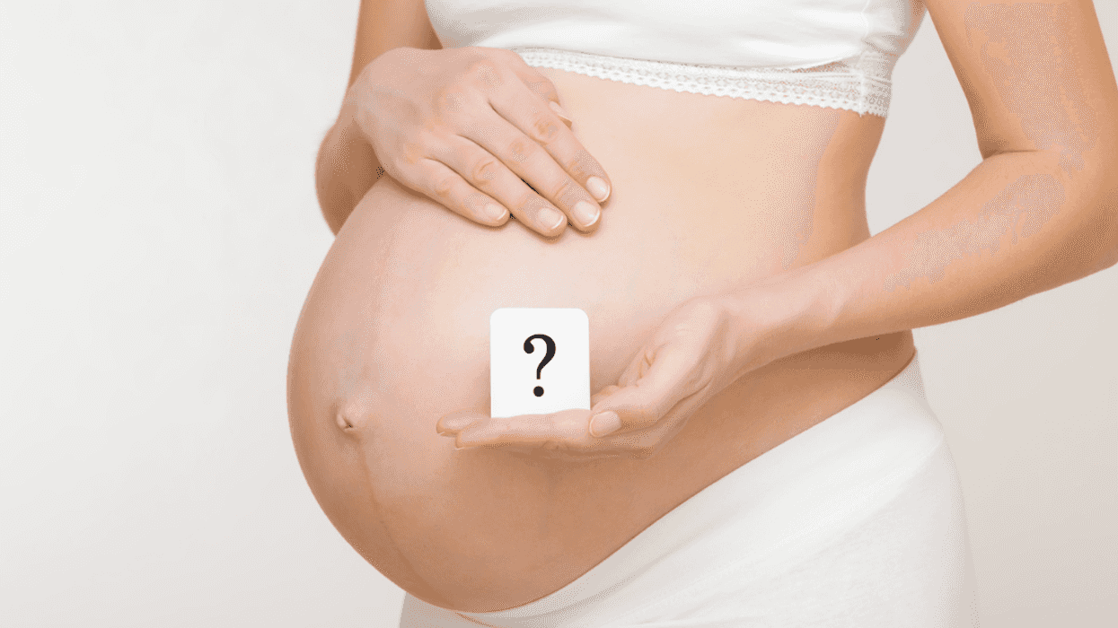 Woman holding a question mark in front of her pregant belly.