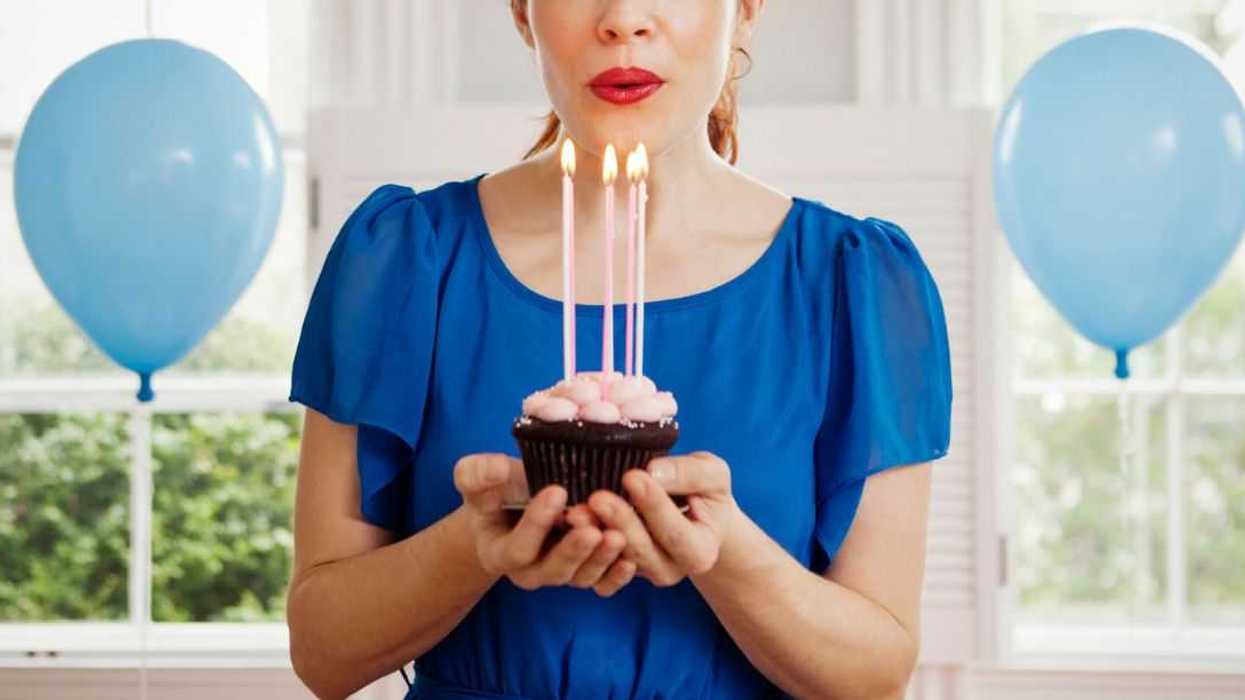 Woman holding cupcake with burning candles at home.