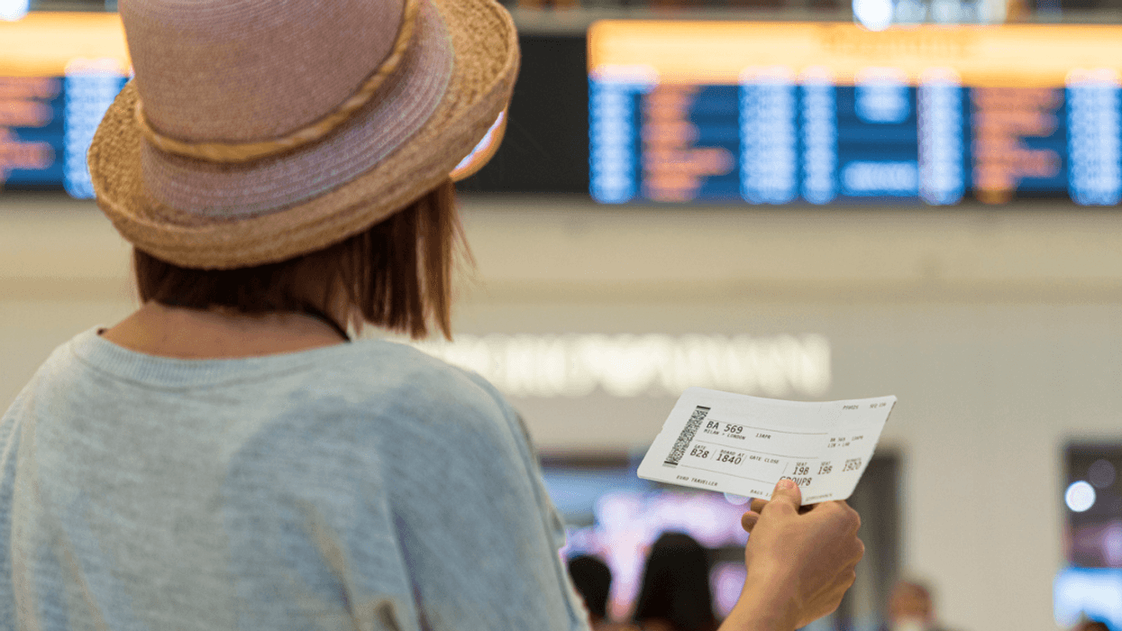 woman holding plane ticket looking at departure board in airport
