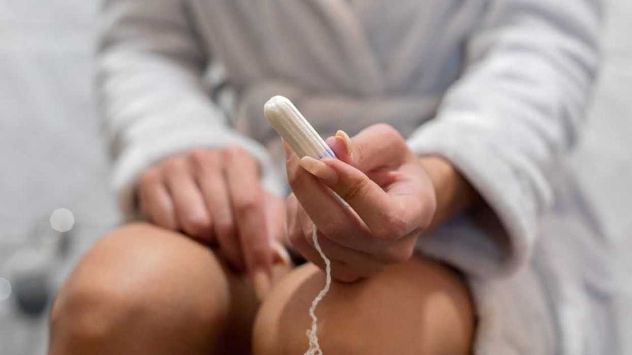 Woman holds a tampon while sitting on the toilet.