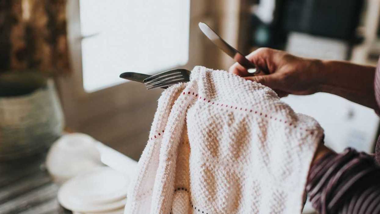 Woman in a kitchen with dish cloth, drying cutlery.