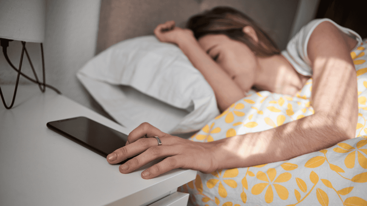 woman in bed turning off the alarm on her phone