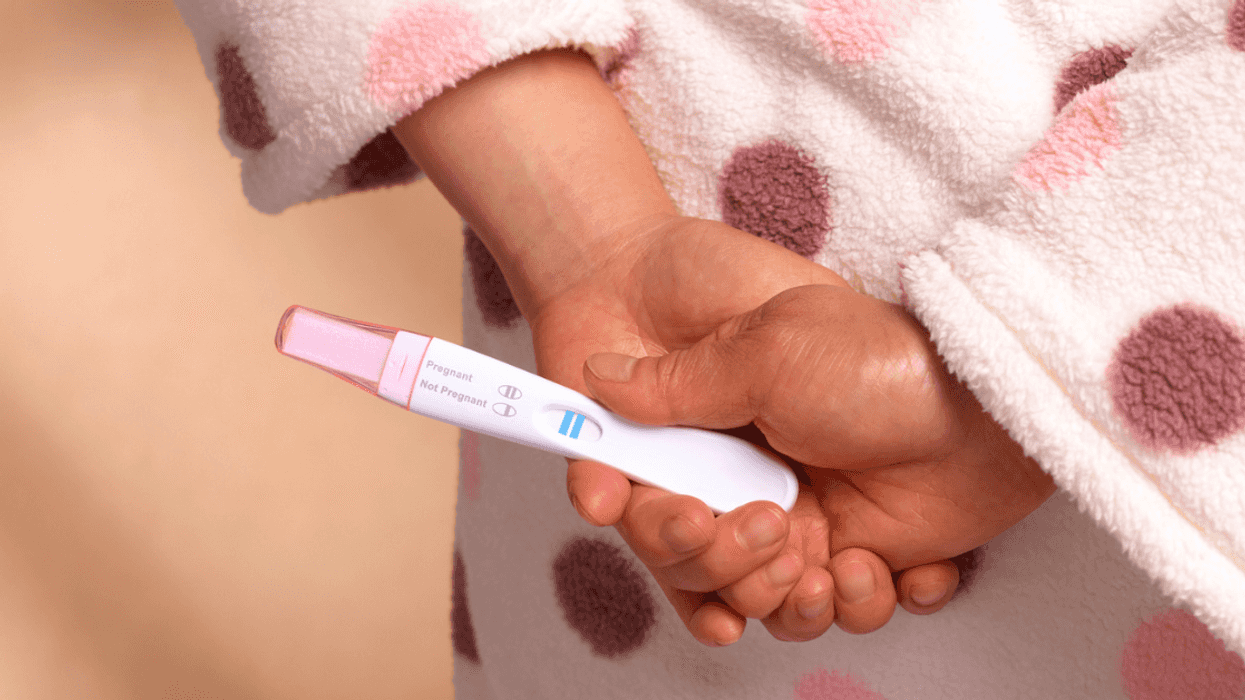 woman in pink bathrobe holding pregnancy test behind her back