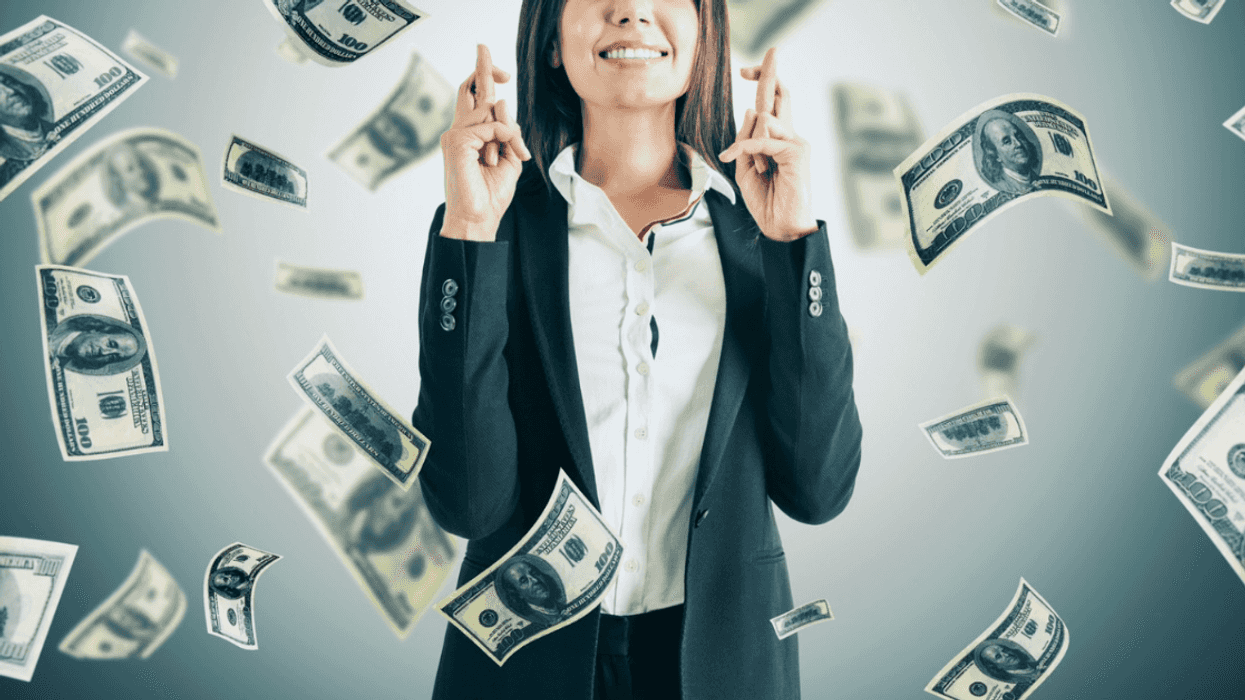 woman in suit standing with fingers crossed as money falls