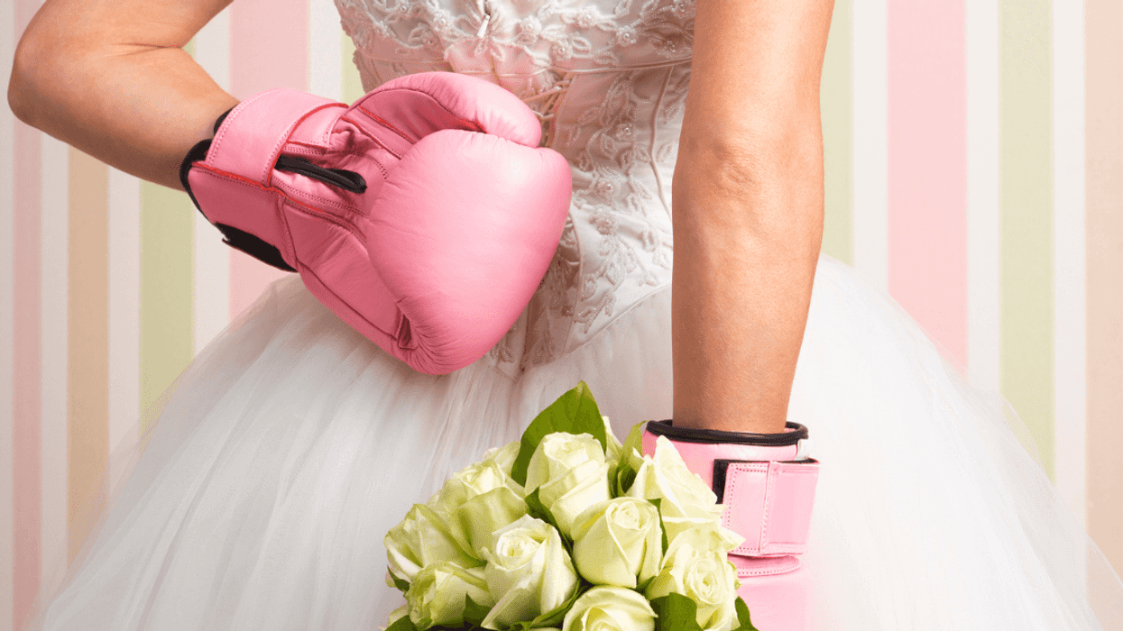 Woman in wedding dress, wearing boxing gloves and holding flowers