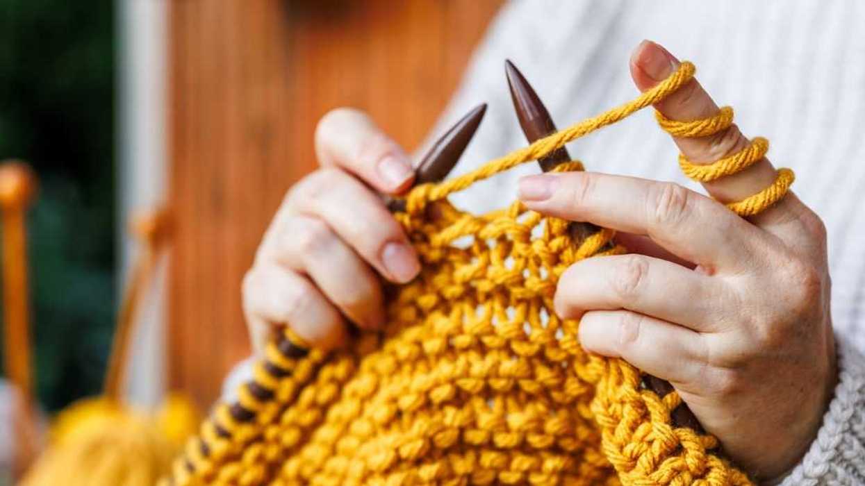 Woman in woollen sweater knits warm clothing of yellow yarn.