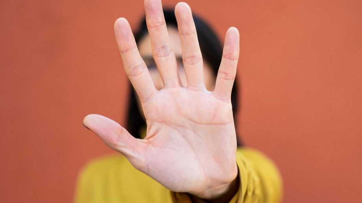 Woman looking at the camera and gesturing to STOP, close up, face obscured by hand