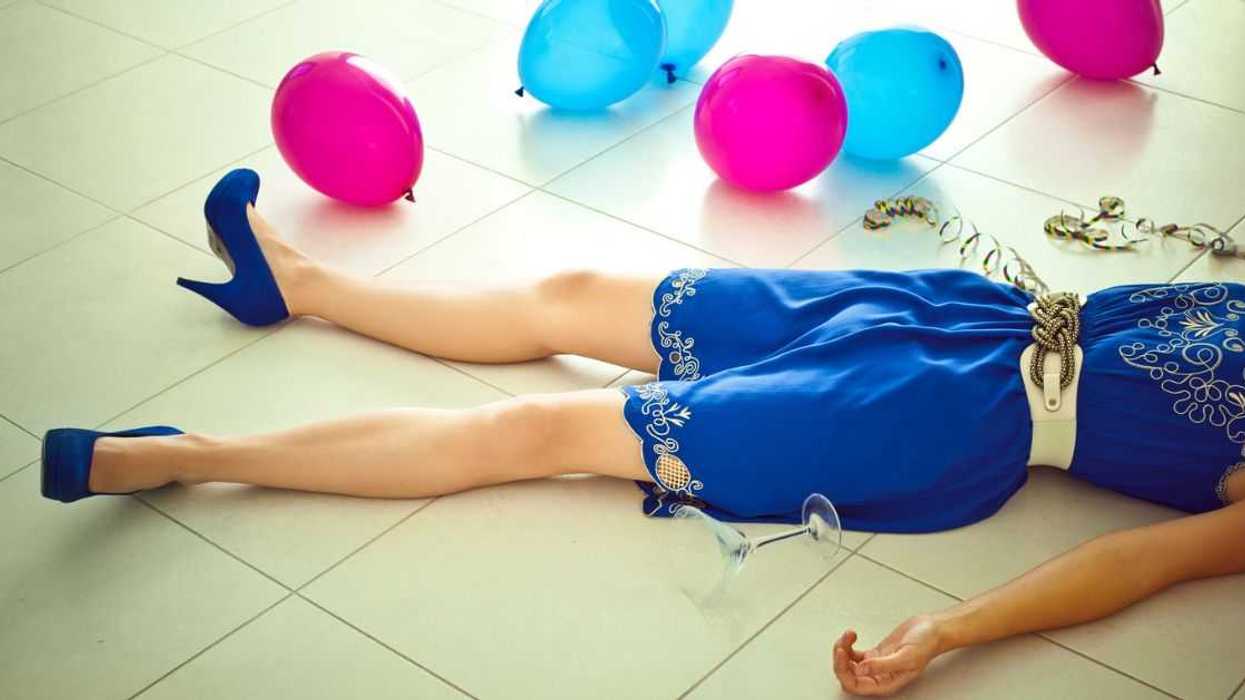 Woman lying down on the floor with balloons and wine glass.