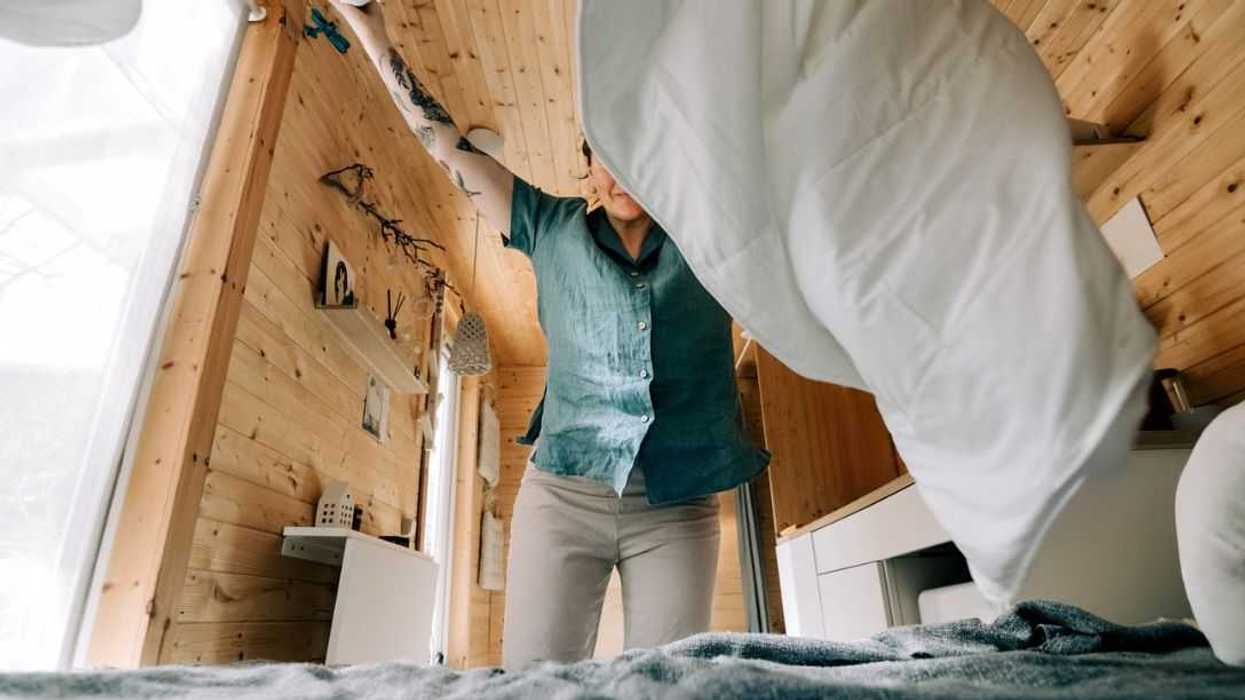 Woman making bed in a cozy, wooden, tiny house.